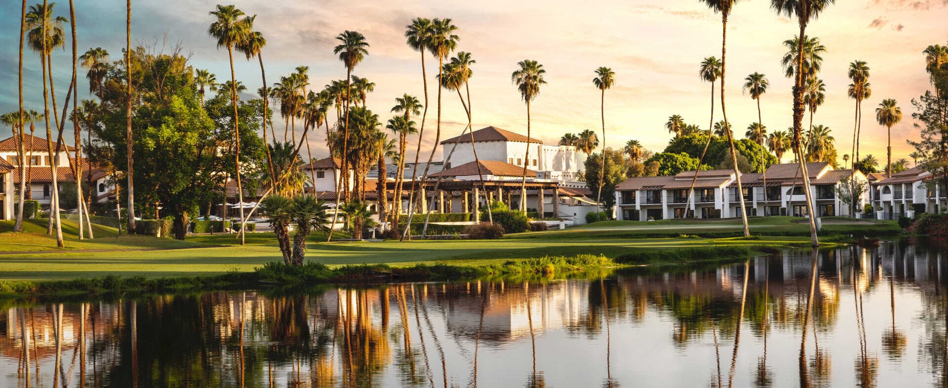 Omni Rancho Las Palmas resort exterior at sunset, framed by palms and reflected in the lagoon